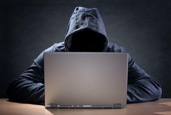 Faceless hacker in hoodie at laptop