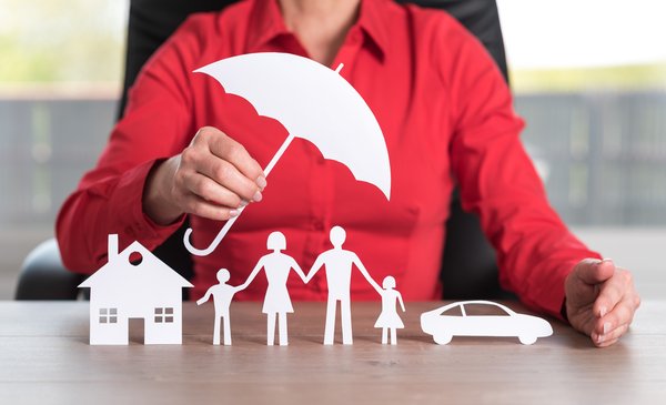 Person holding paper cutout of umbrella over paper cutout family and house.