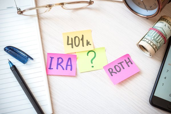 Sticky notes with 401k, IRA, Roth, and a question mark on a desktop.