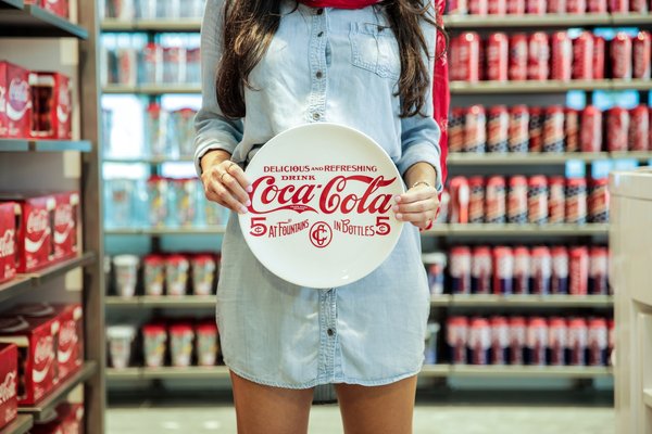 Person holding a Coca-Cola plate inside a Coke store.