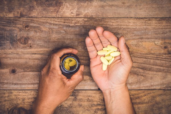 Hands holding some pills from a bottle over a wooden table.