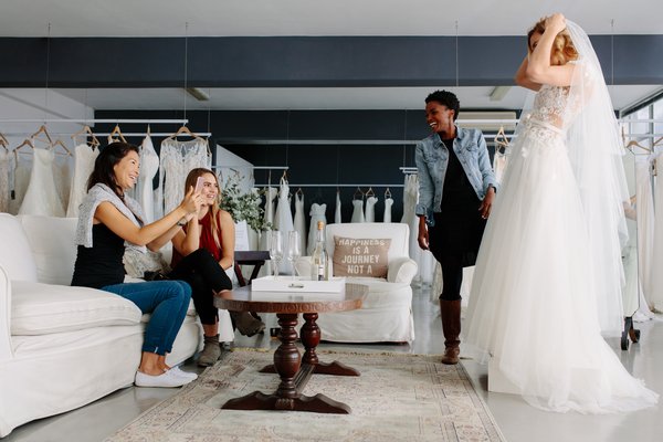 A woman tries on a wedding dress in a shop with friends.
