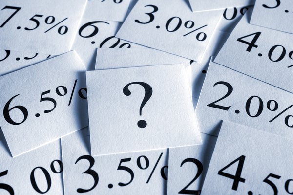 A pile of square pieces of paper with an interest rate written on each and one in the middle with a question mark on it.