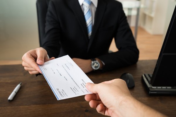 A hand holds out a check to a man in a business suit.