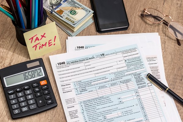 Tax documents on a desk with a pen, calculator, and note that says Tax Time.
