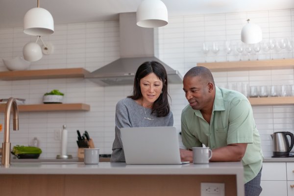 Two people in kitchen looking at laptop.