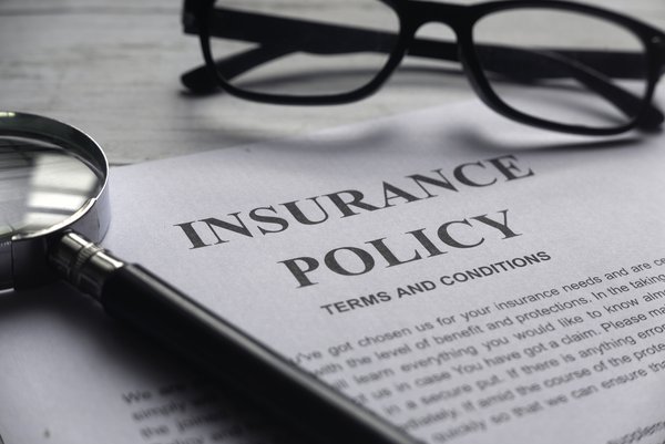 A pair of glasses and a magnifying glass atop a document that says Insurance Policy.