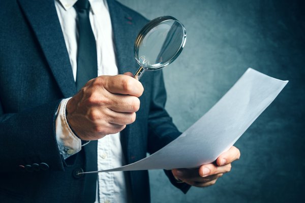 A person inspects a document with a magnifying glass.