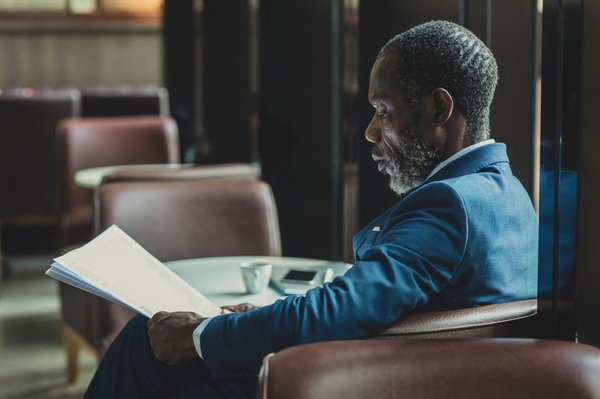 African businessman wearing suit and tie sitting at coffee shop and reading daily newspaper.