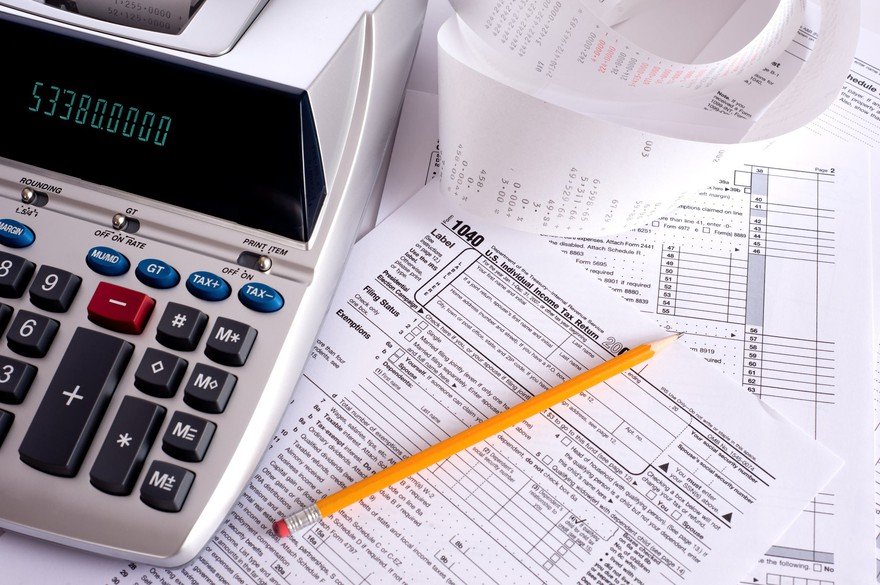 An adding machine and pencil on top of a pile of tax forms.