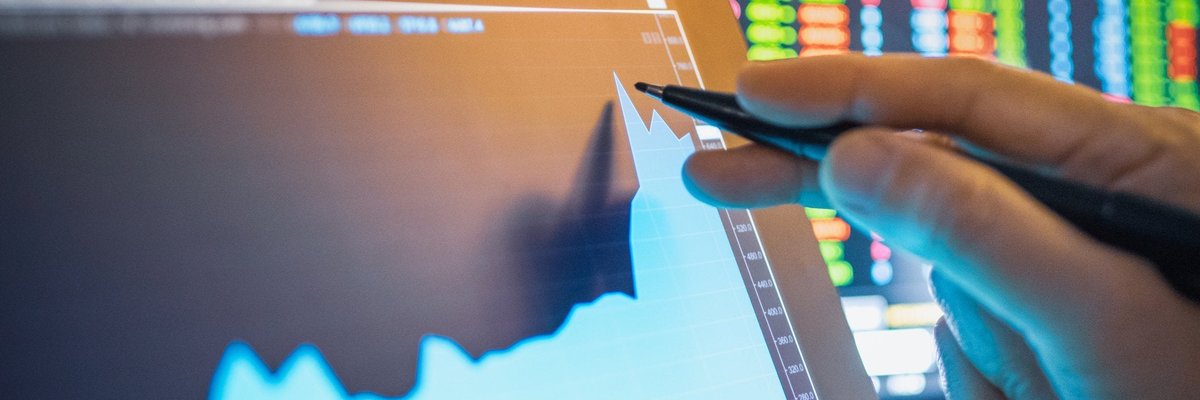 Person using pen to point to rising graph of computer screen.