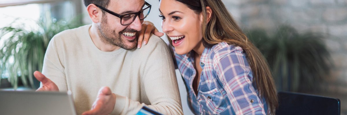 Young couple appear to be pleased about something they're viewing on a laptop while woman holds a credit card.