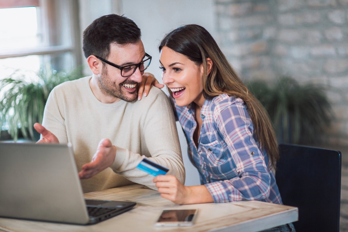 Young couple appear to be pleased about something they're viewing on a laptop while woman holds a credit card.