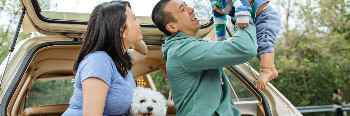 A couple smile and enjoy the day with their baby and two dogs.