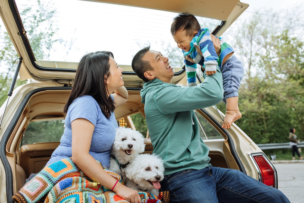 A couple smile and enjoy the day with their baby and two dogs.