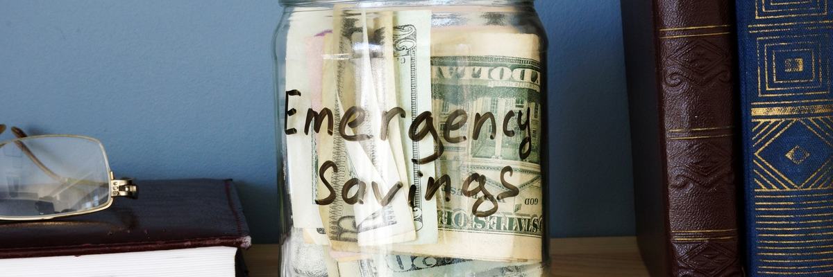 A jar that says emergency savings is on a bookshelf and full of cash.