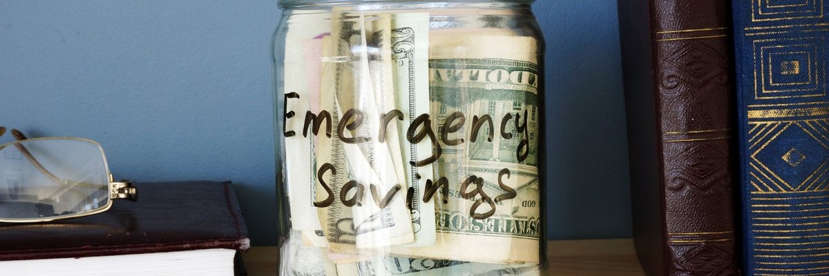 A jar that says emergency savings is on a bookshelf and full of cash.