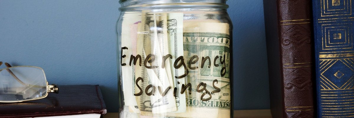 A jar that says emergency savings is on a bookshelf and full of cash.
