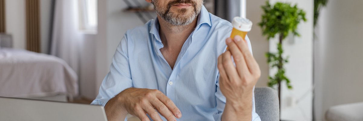 Adult person using laptop and looking at a prescription medication bottle.