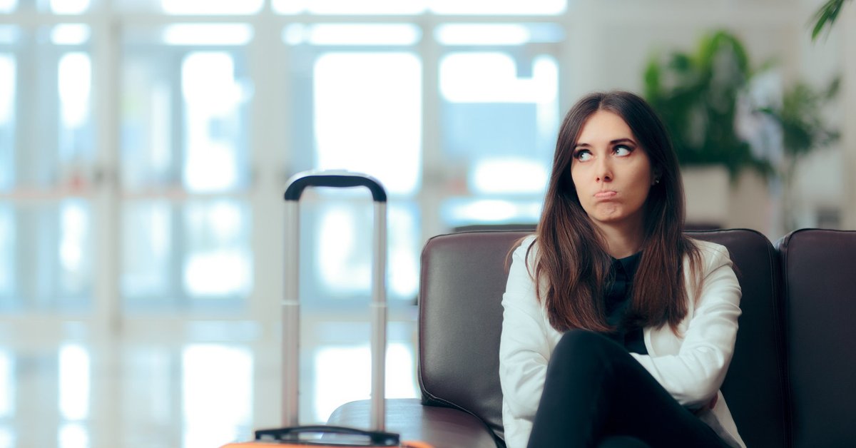 An unhappy woman sitting in an airport next to her suitcase.