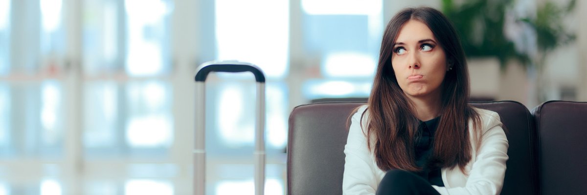 Disappointed woman sitting in airport chair next to her luggage.