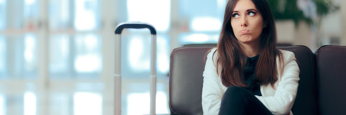 Disappointed woman sitting in airport chair next to her luggage.