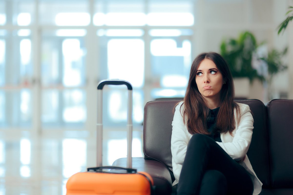 An unhappy woman sits next to her luggage in an airport.