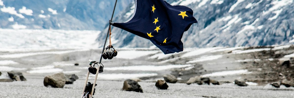The state flag of Alaska fluttering in front of a mountainous open space..