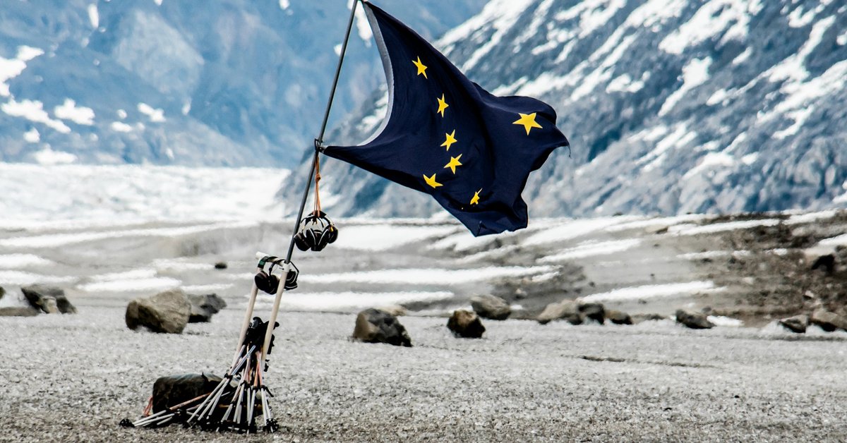 The state flag of Alaska fluttering in front of a mountainous open space..