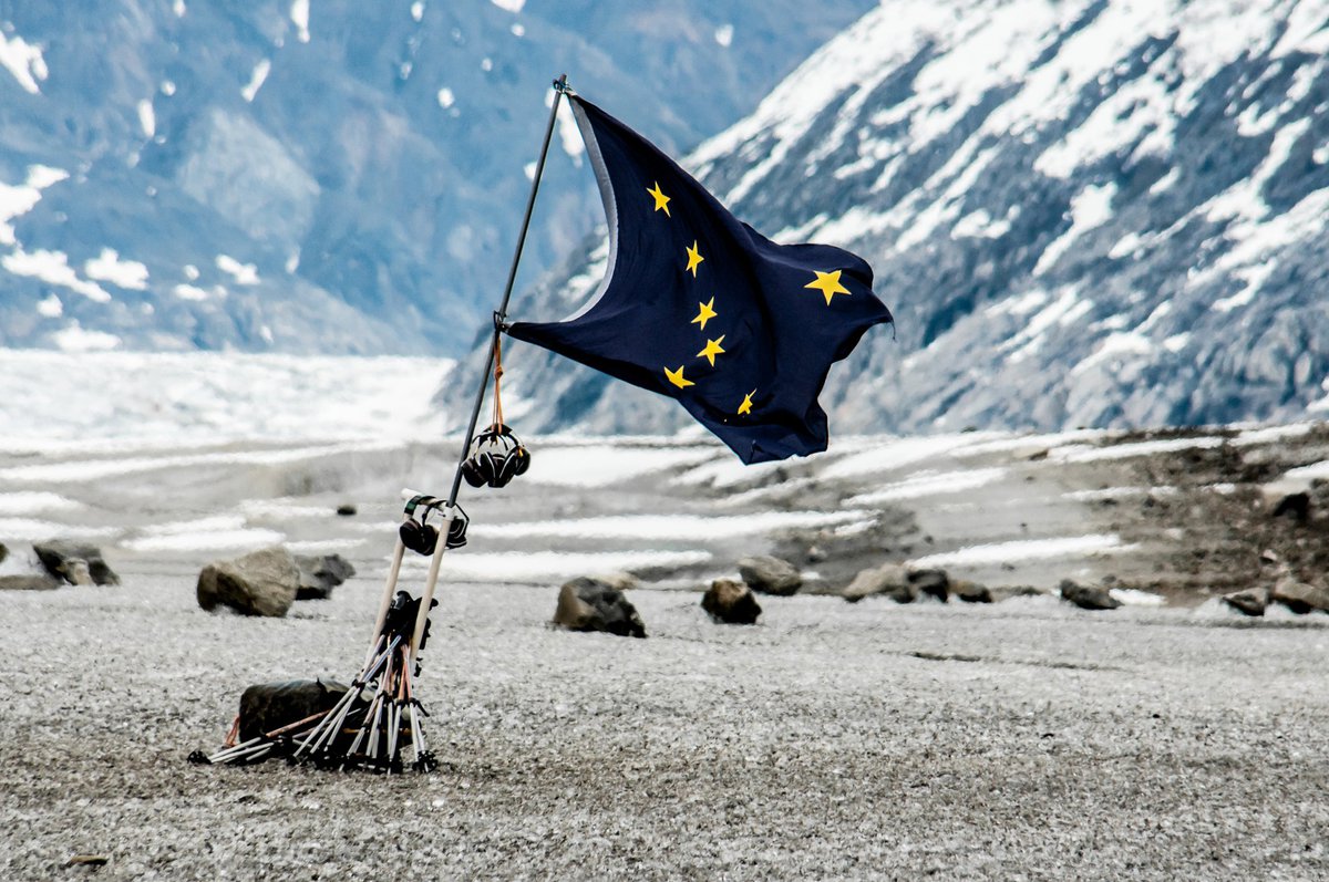 The state flag of Alaska fluttering in front of a mountainous open space..