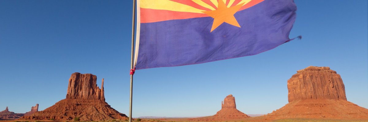 The Arizona state flag flying in front of rock formations in the desert.