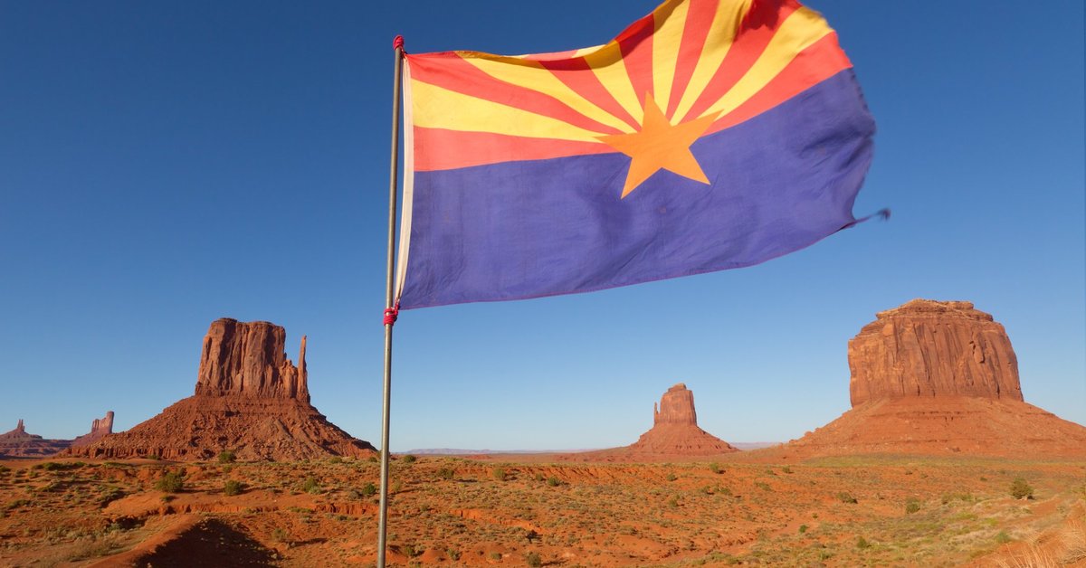 The Arizona state flag flying in front of rock formations in the desert.