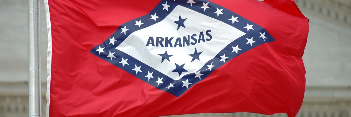 The Arkansas state flag flying in front of a courthouse.