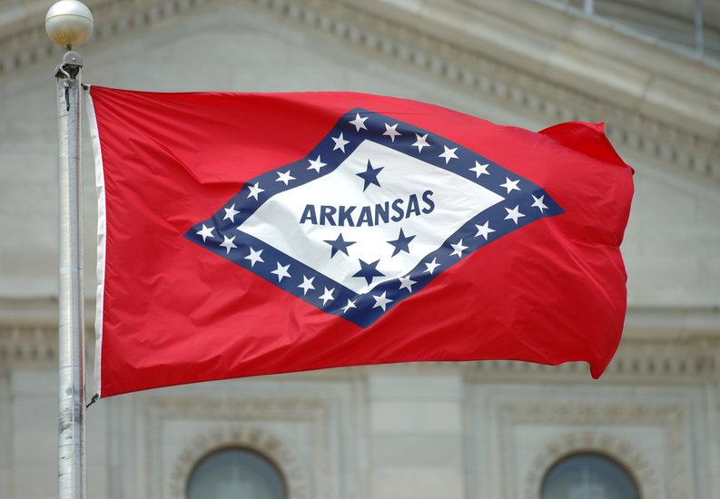 The Arkansas state flag flying in front of a courthouse.