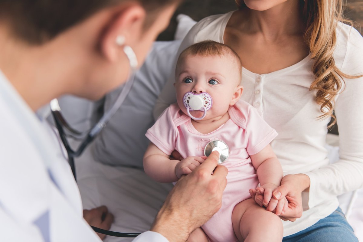 Baby in mother's lap staring up at doctor.