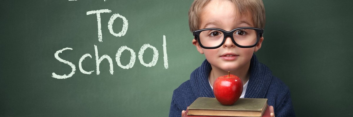 A child holding books and an apple in front of a chalk board that says Back To School.
