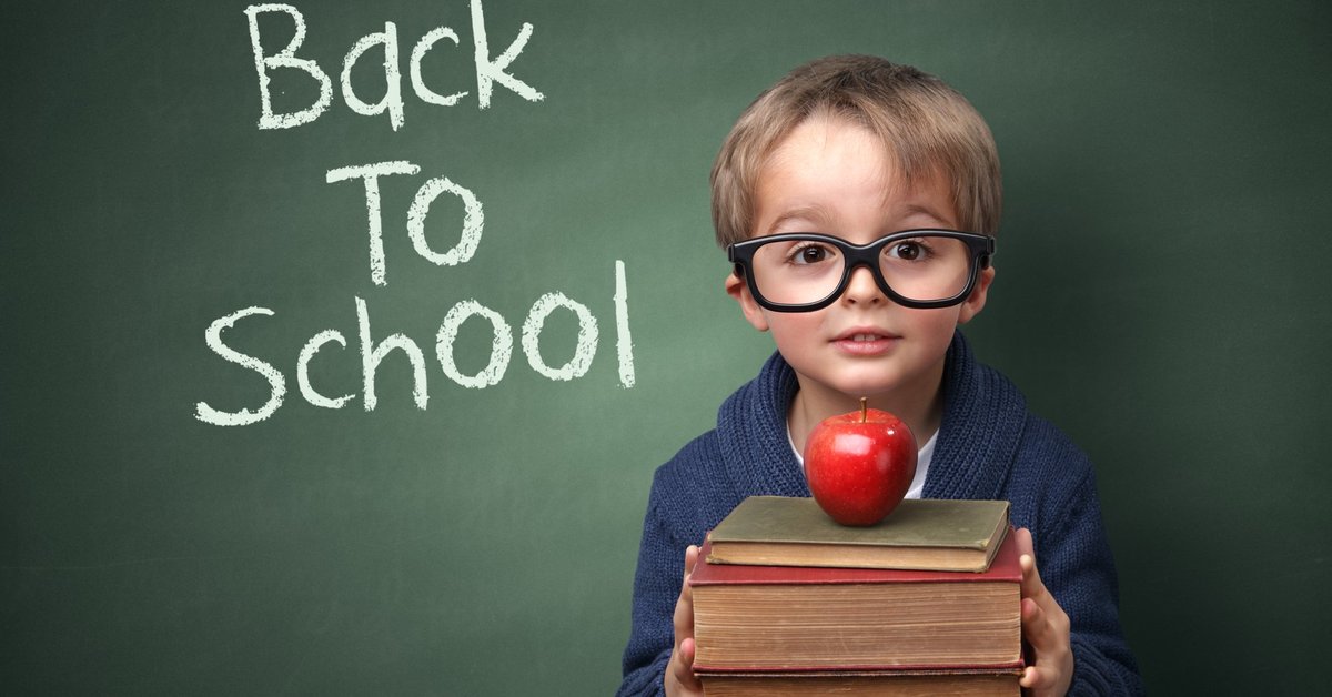 A child holding books and an apple in front of a chalk board that says Back To School.