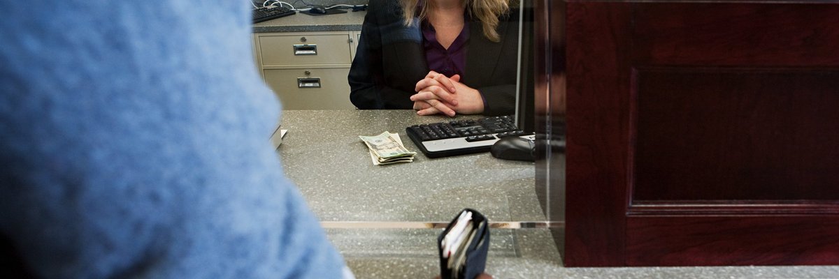 A bank teller smiles to a customer from behind her desk.