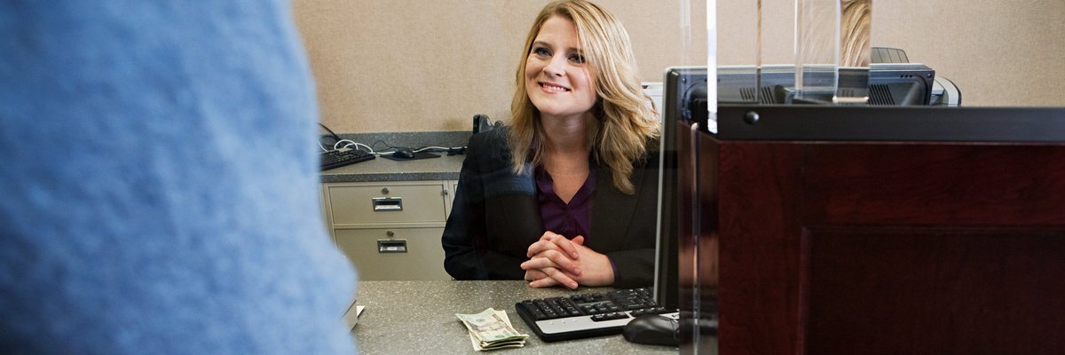 A bank teller smiles to a customer from behind her desk.