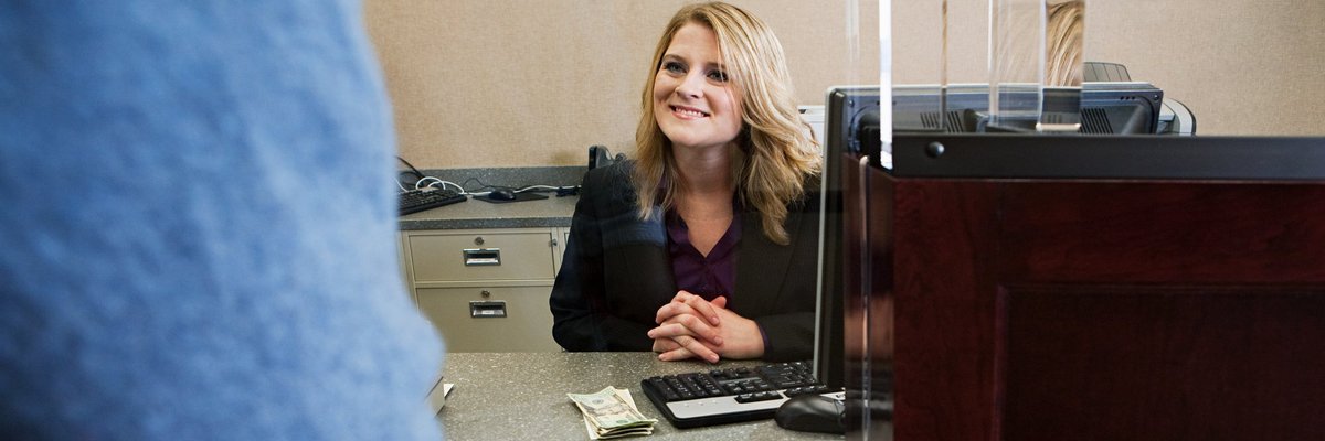 A bank teller smiles to a customer from behind her desk.
