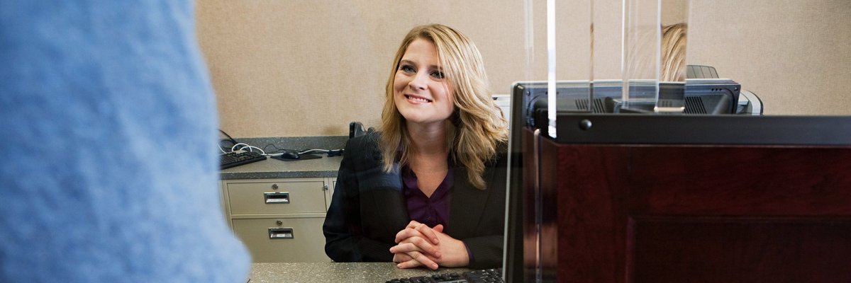 A bank teller smiles to a customer from behind her desk.