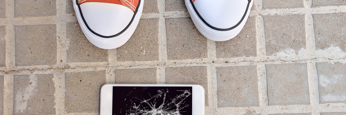 Someone standing next to a dropped cell phone with a broken screen.