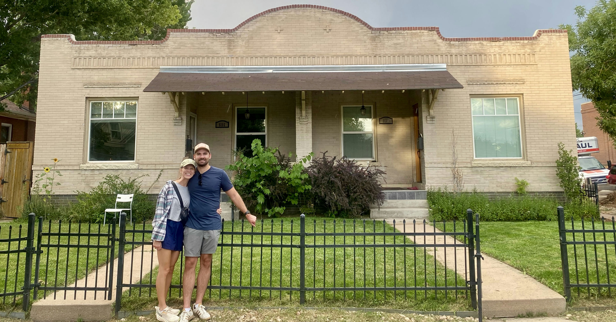 Brooklyn and husband standing in front of gated house with rainbow in the background.