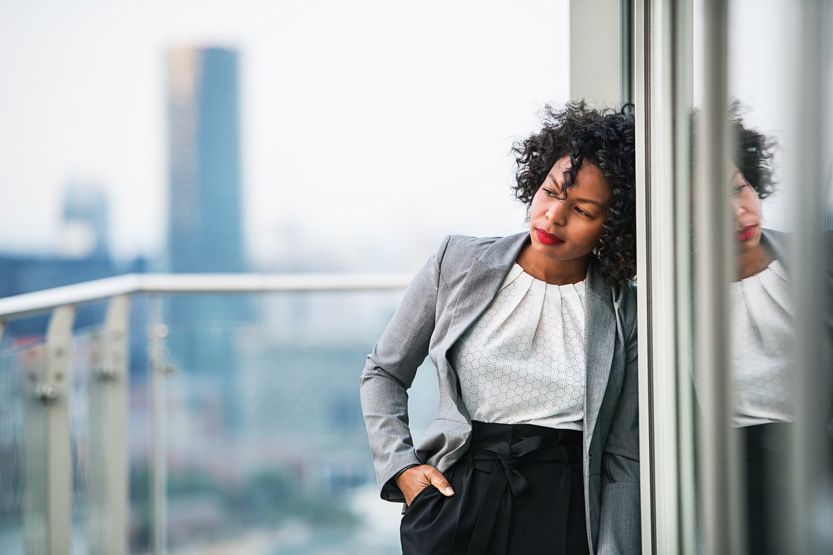 A businesswoman standing on a balcony looking thoughtful.
