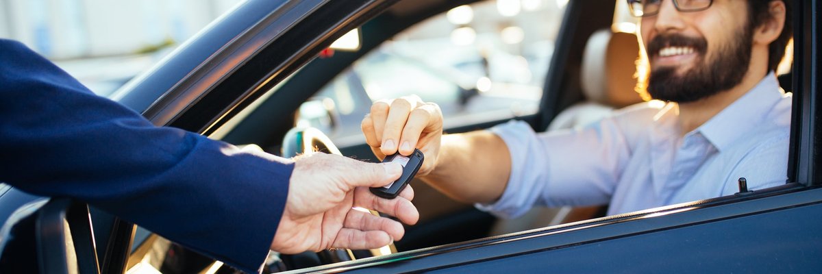 man sitting in car as salesman hands him the key through the window