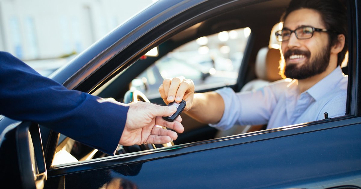 man sitting in car as salesman hands him the key through the window