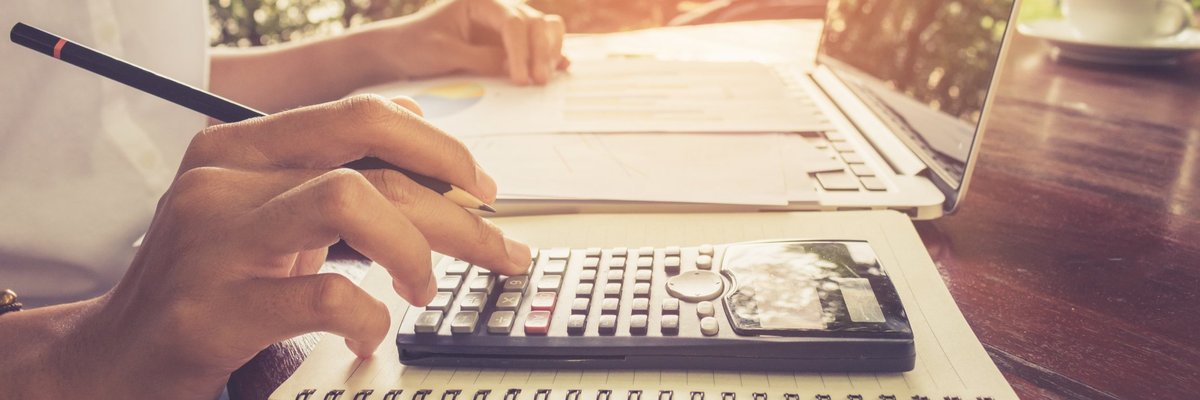 A person using a calculator and laptop at a sunny cafe.