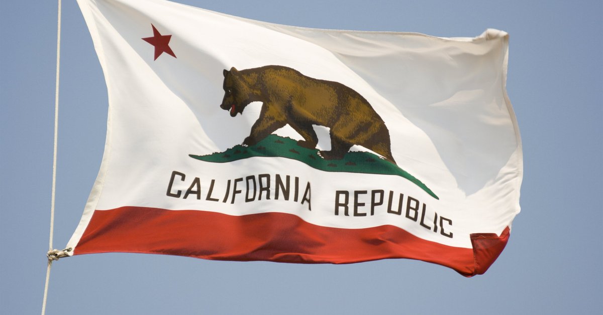 The California state flag fluttering in front of a blue sky.