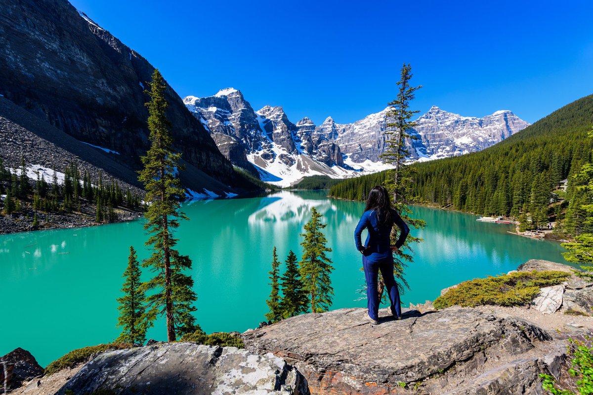 Woman looking out over a blue lake and mountains.