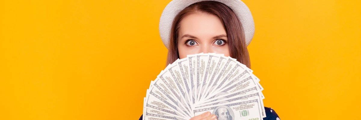 A young woman wearing a hat holds a fan of hundred dollar bills.